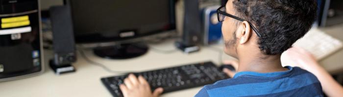 Teenage boy in a blue shirt working on a computer.